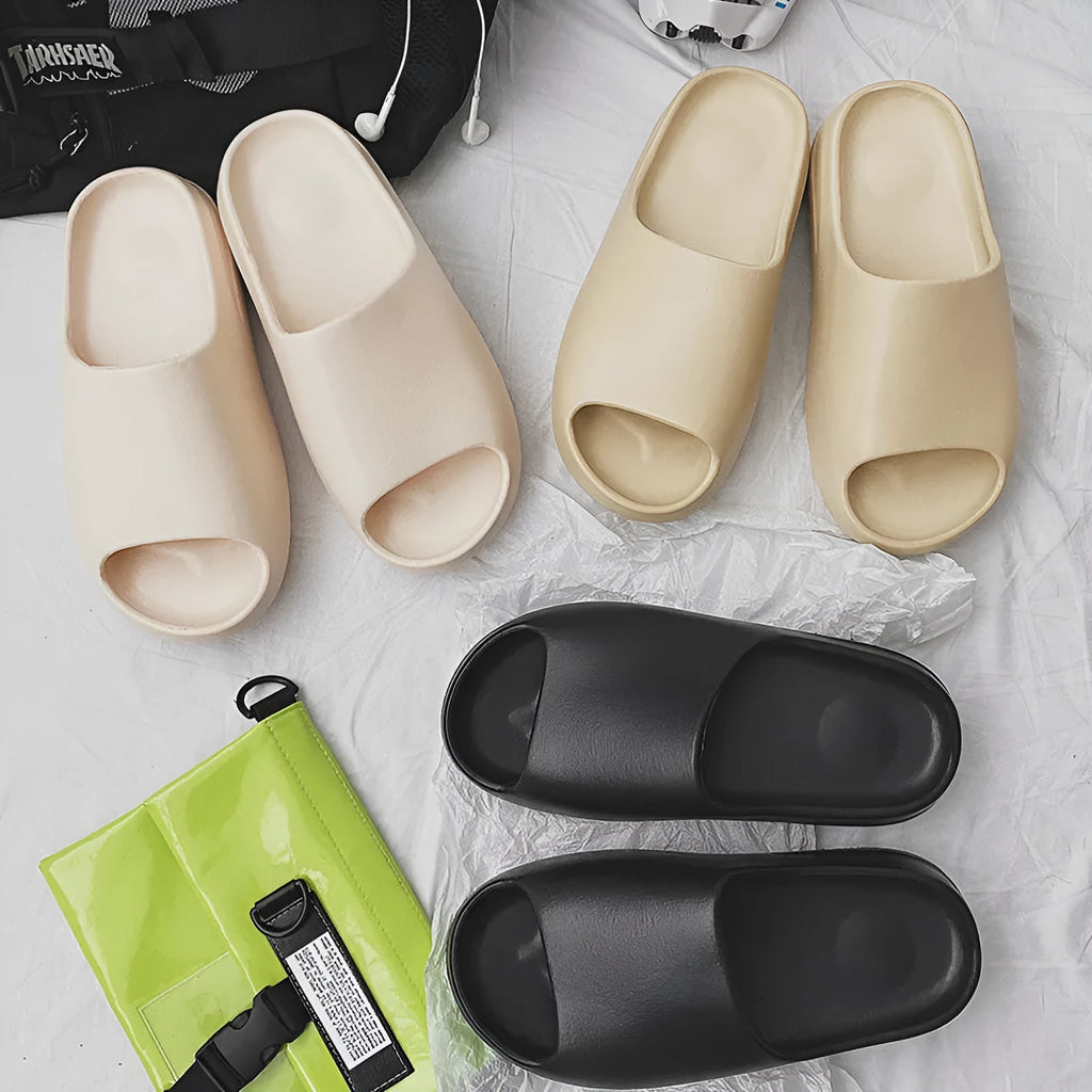 Women's black beach slippers with thick EVA soles on a sandy background.