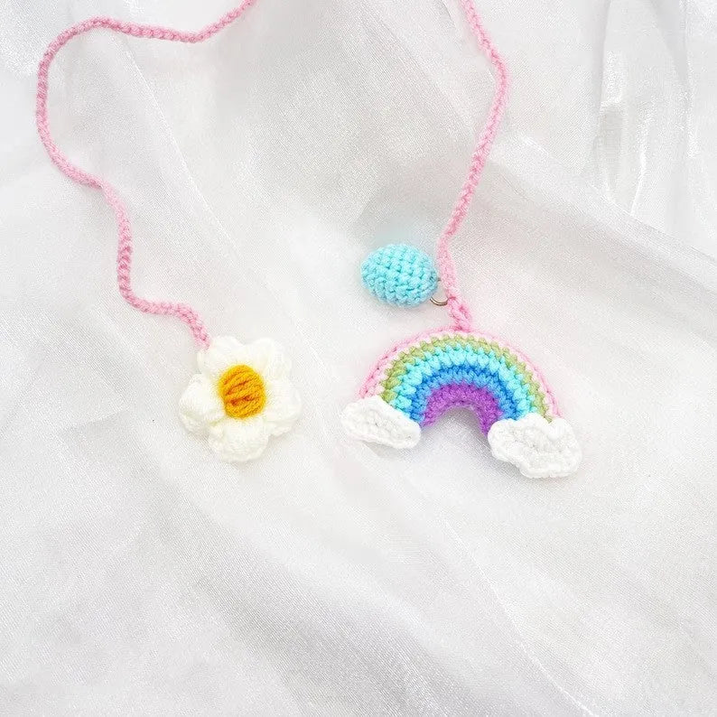 Handmade crocheted avocado-shaped car pendant with a rainbow flower on a green background.