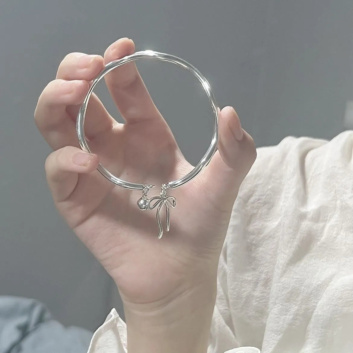 Silver adjustable bracelet with bow detail and bell opening clasp on wrist