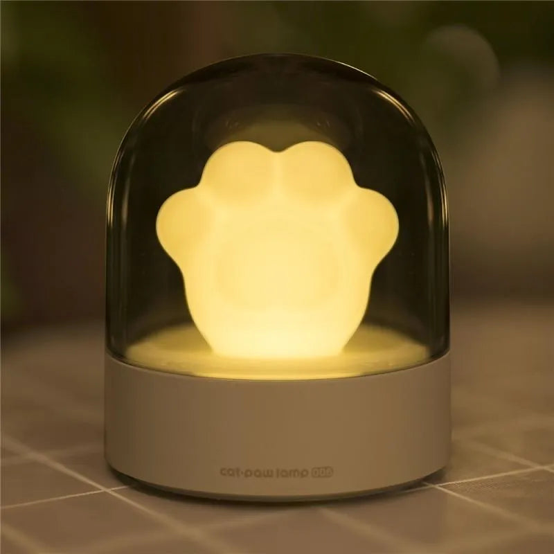 Grey cat paw shaped USB rechargeable night light with music box on a desk.