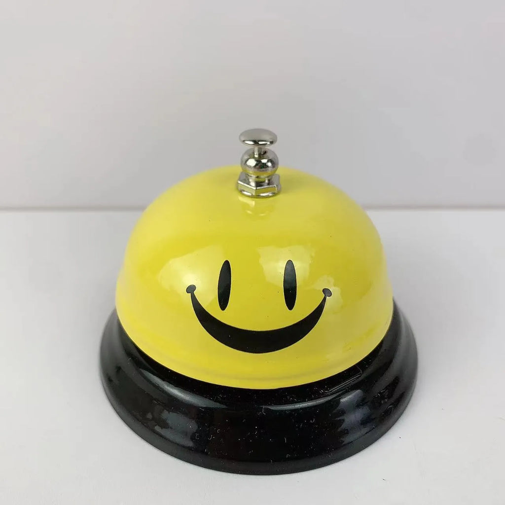 Iron table serving bell in multiple colour options on a wooden surface.