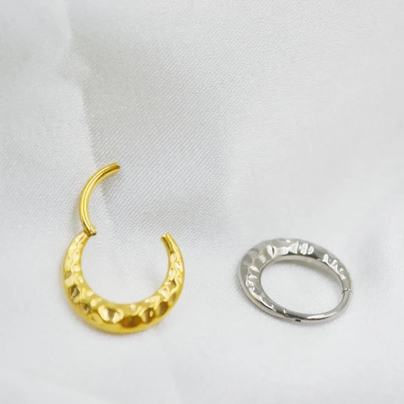 Close-up of a titanium concave-convex nose ring in gold, showing its carved texture and circular shape.