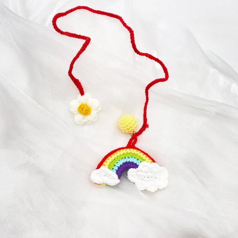 Handmade crocheted avocado-shaped car pendant with a rainbow flower on a green background.
