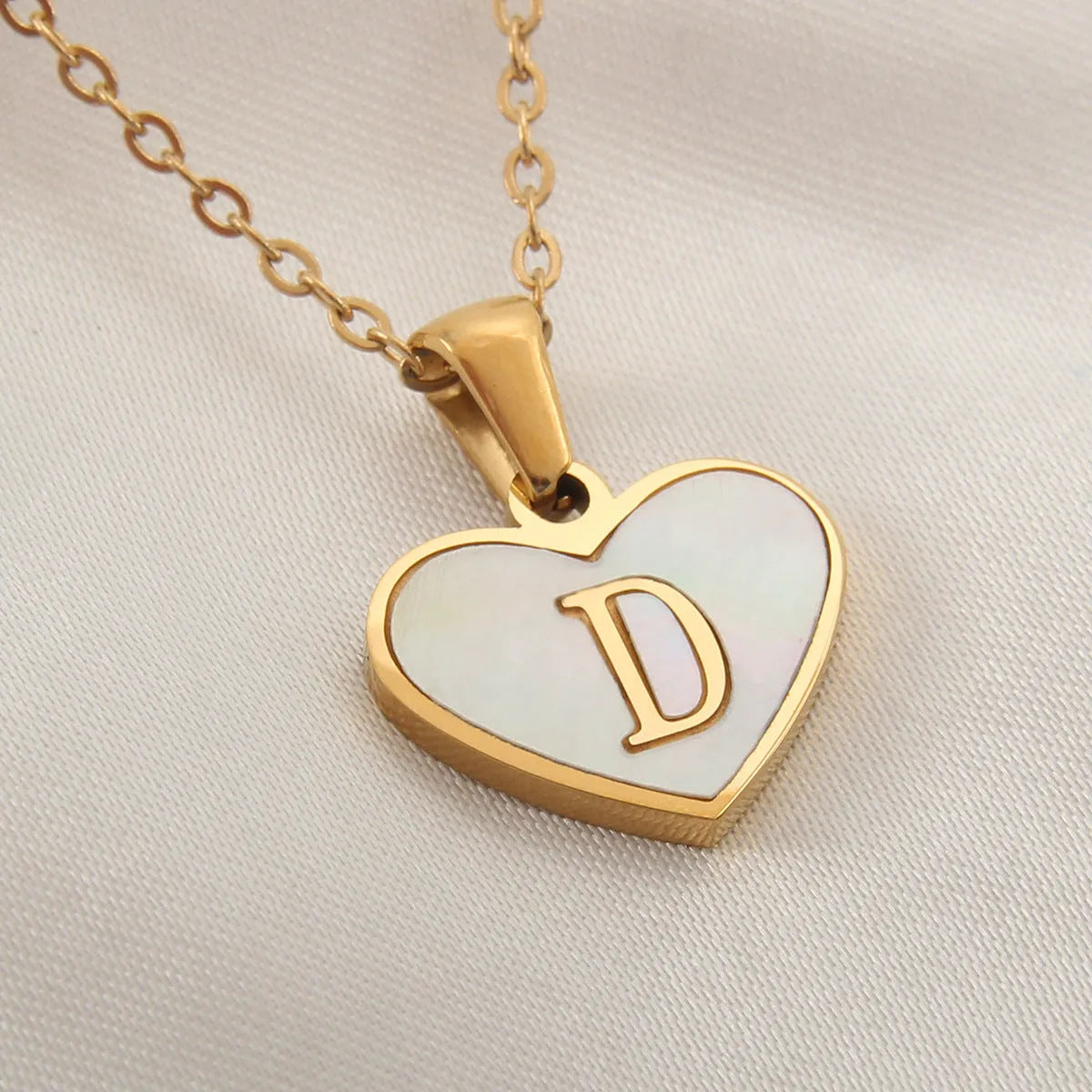 Gold-plated heart necklace with white shell pendant showing initial engraving on stainless steel chain