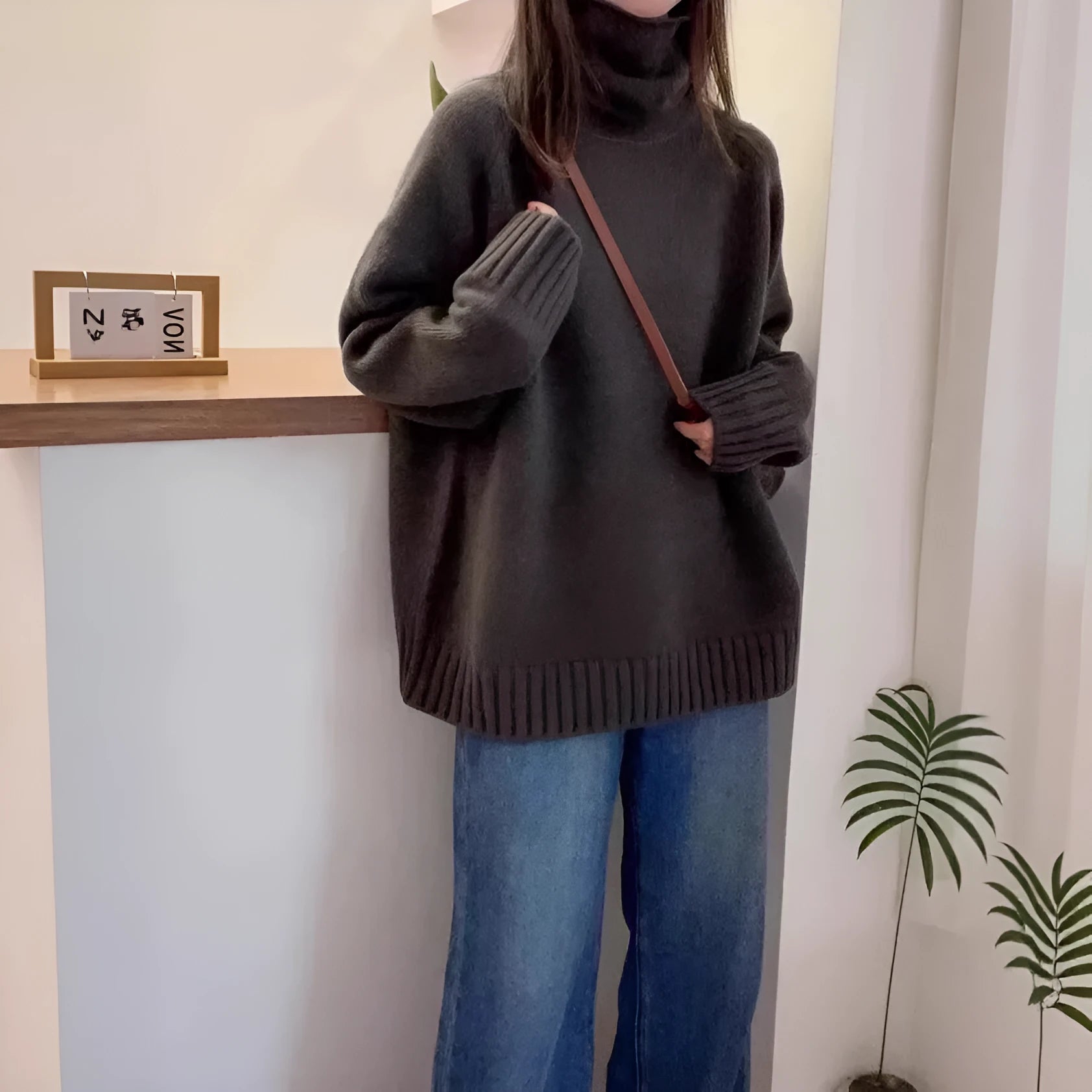 Women's loose grey turtleneck sweater with thick curling pile collar, worn in a casual setting.