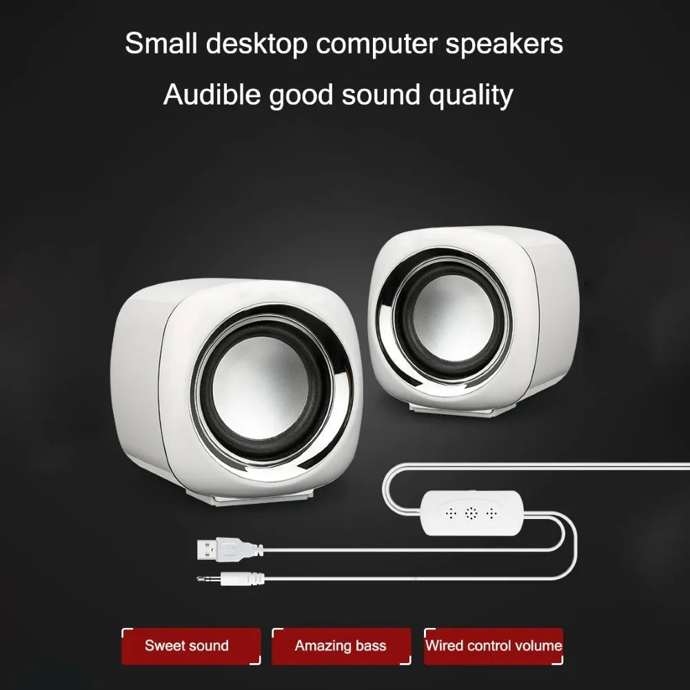 A pair of compact black wired desktop computer speakers with a 3.5mm audio cable on a wooden desk