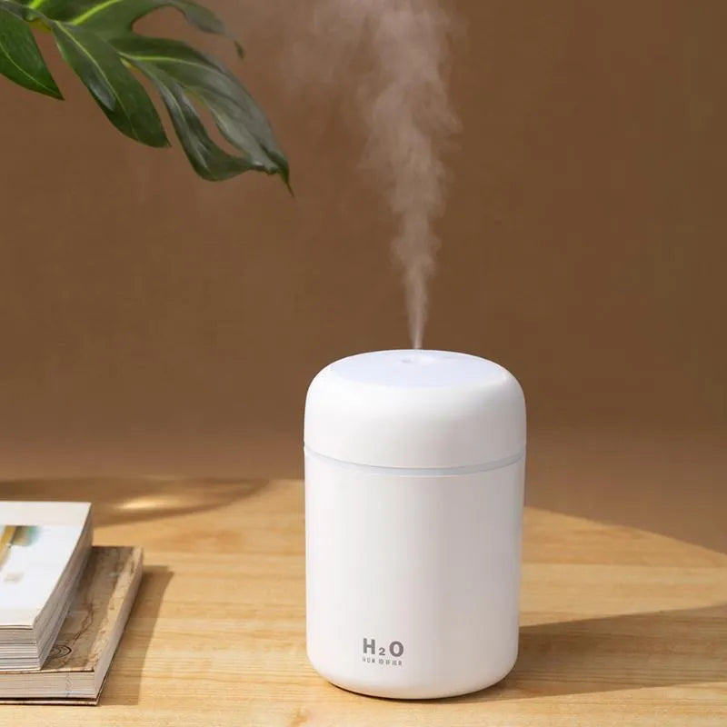 Pink USB mini humidifier with LED lights on wooden desk beside laptop