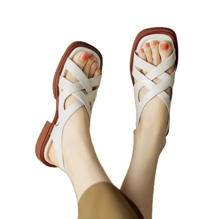 Women's black patent leather square toe sandals with cross strap on a white background.