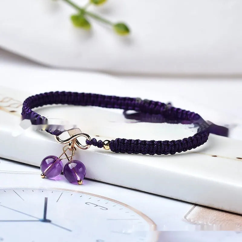 Close-up of a women's natural crystal bracelet with a detailed cherry charm in strawberry quartz colour.