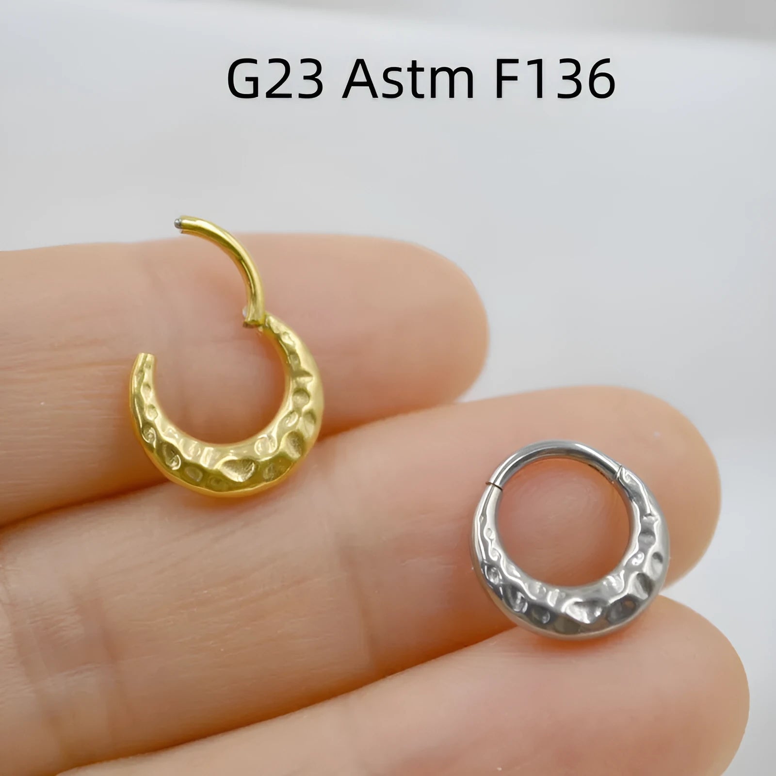 Close-up of a titanium concave-convex nose ring in gold, showing its carved texture and circular shape.