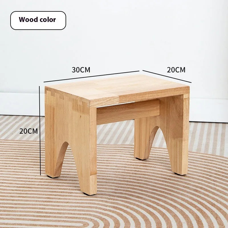 Solid wooden shoe changing stool with a distressed finish, shown in a living room setting.