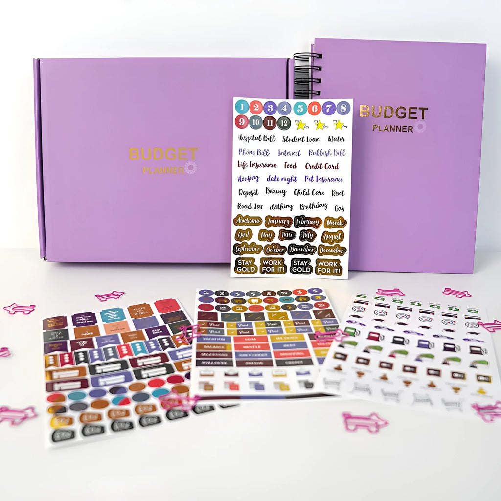 J12 Purple coil-bound monthly financial planning notebook with pen, stickers, and paper clips on a desk.