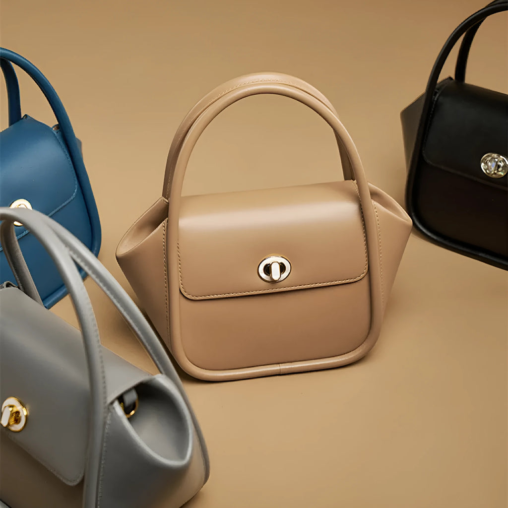 Brown leather wing-shaped tote bag with a buckle detail and latch closure, shown with a single cross-body strap.