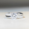 Silver ring with a 1 karat moissanite stone in a four-claw setting and a geometric twisted arm band.