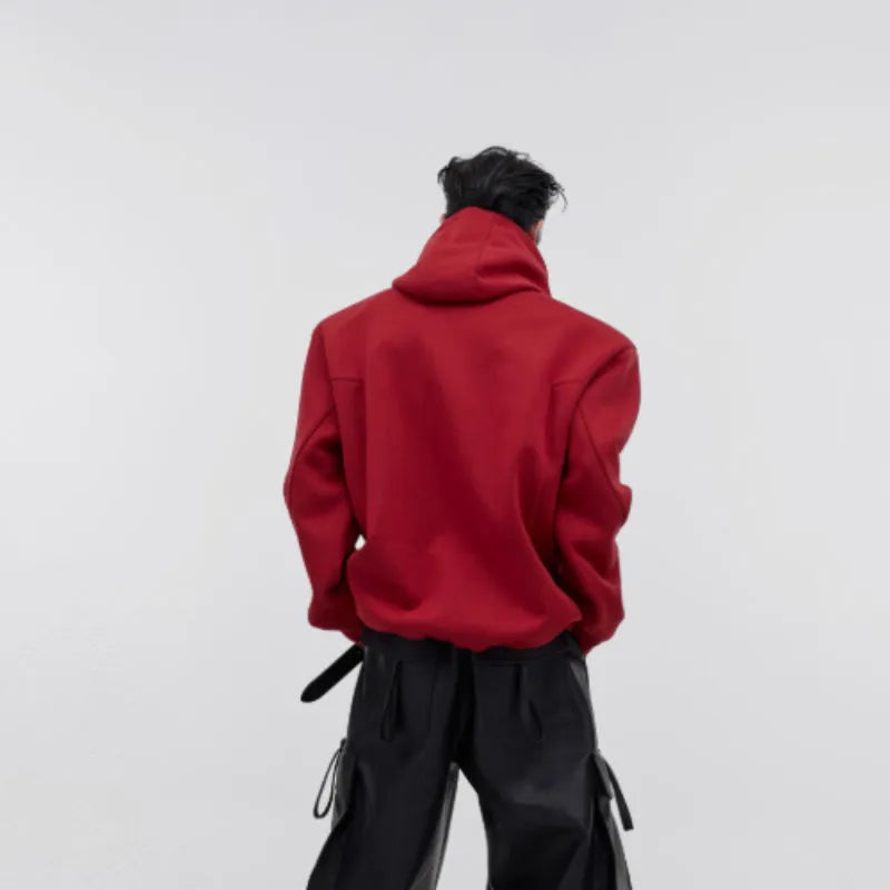 Man wearing a loose black hooded sweater with metallic 3D printed design and structured shoulder pads.