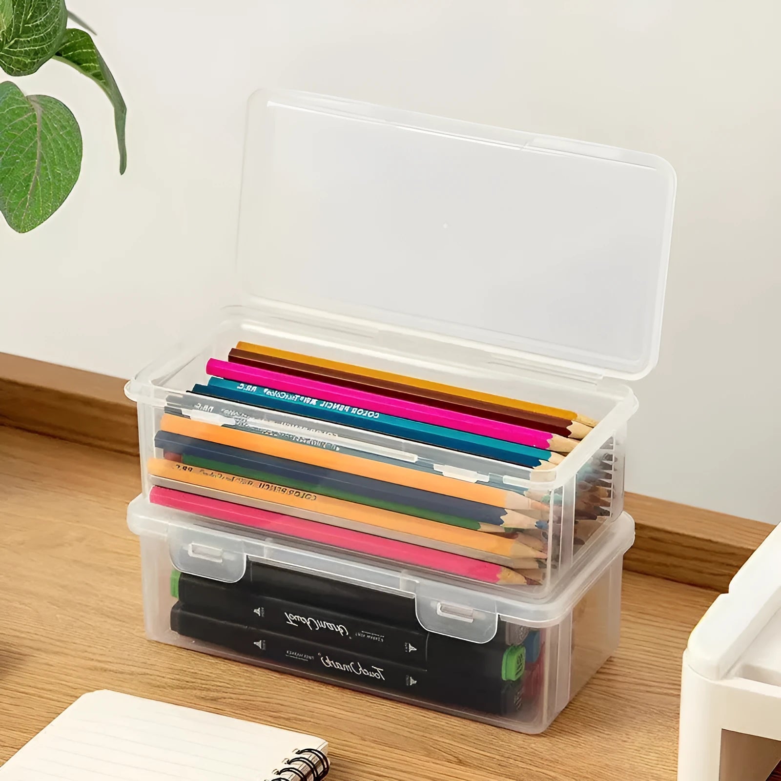 Clear plastic storage box for pencils, colouring leads, and children's crayons on a desk.
