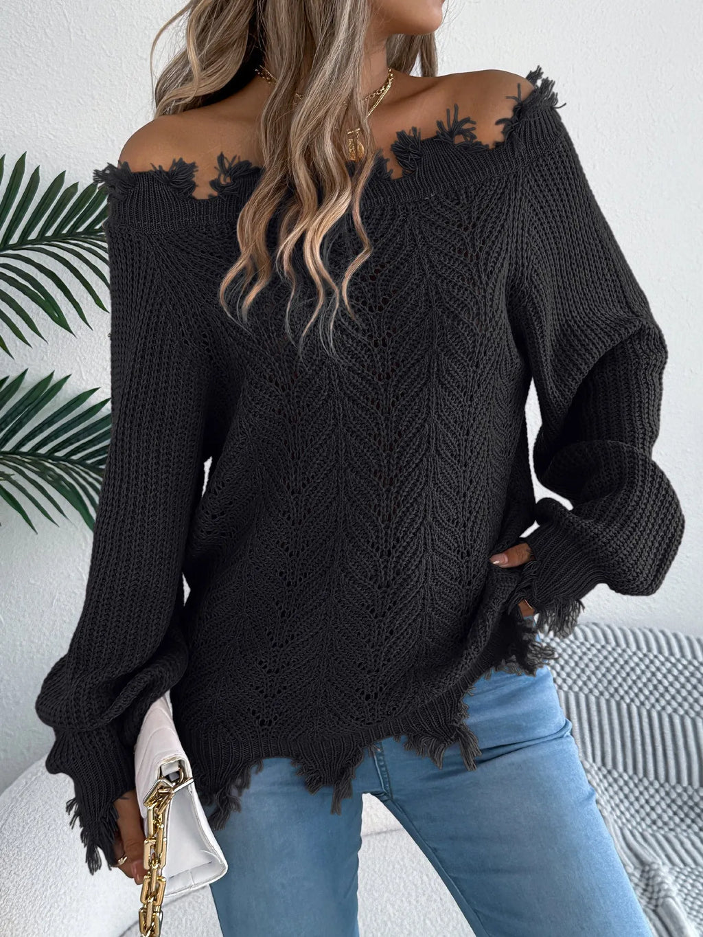 White hollow-out cut off-the-shoulder pullover sweater with long sleeves on a hanger.