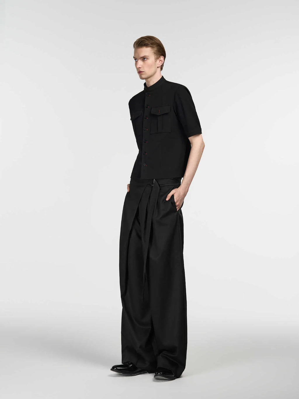 Black loose fit straight leg trousers with a single pleat and adjustable waistband on a hanger.