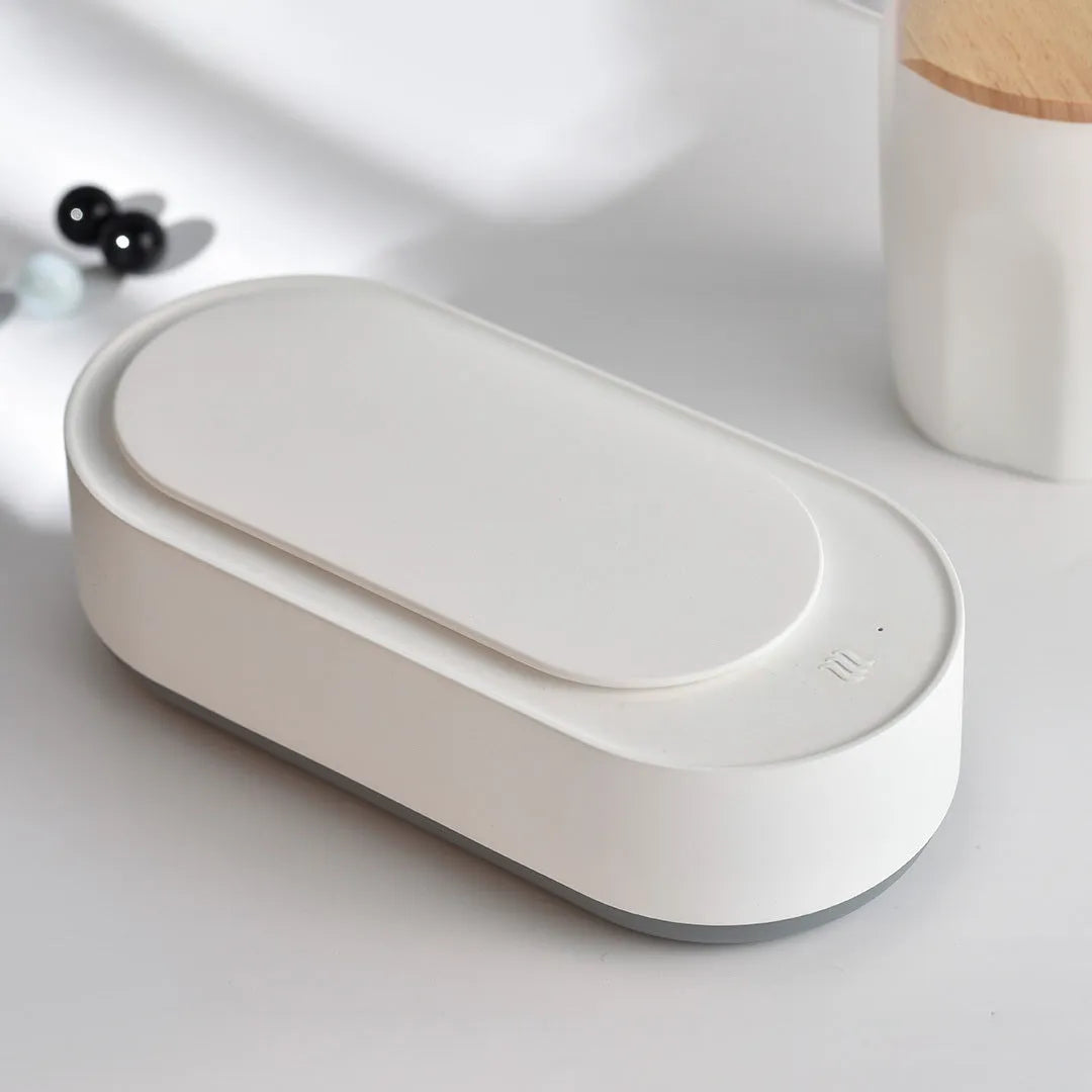 White portable ultrasonic cleaner with stainless steel tank and a single control button.