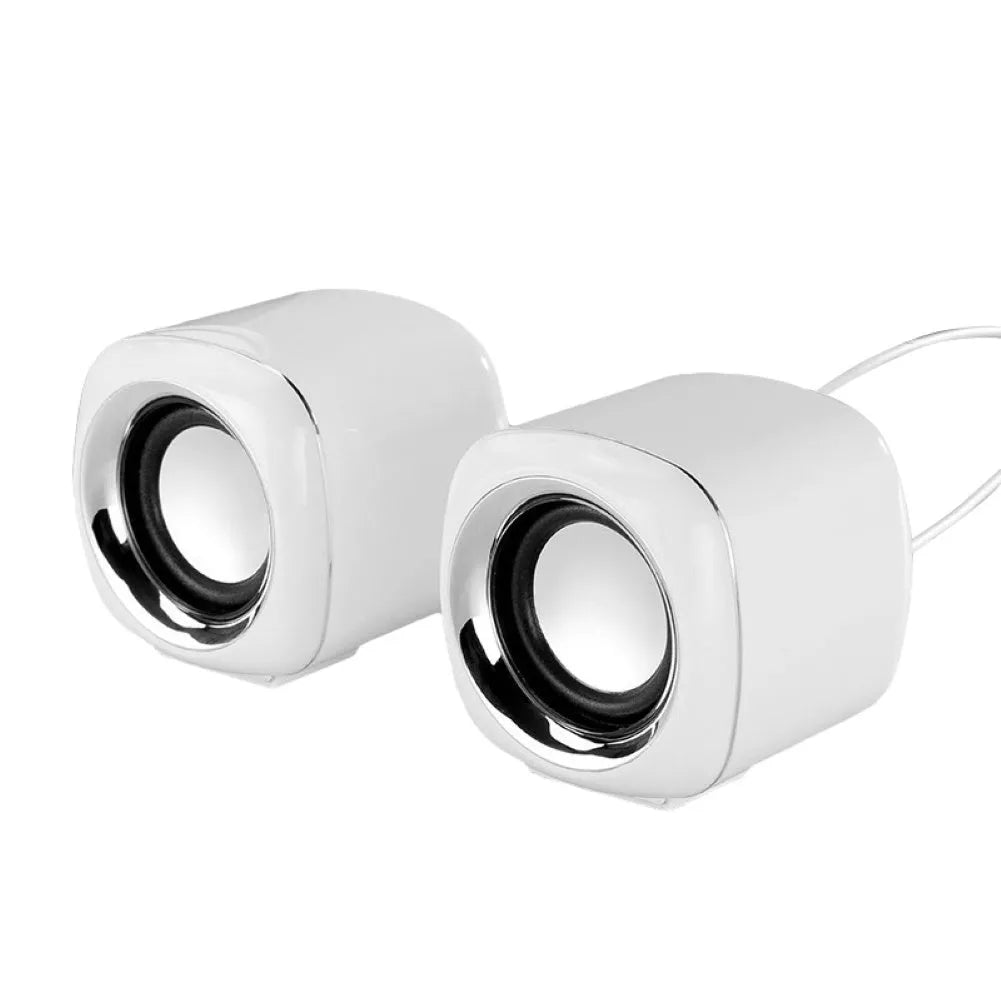 A pair of compact black wired desktop computer speakers with a 3.5mm audio cable on a wooden desk