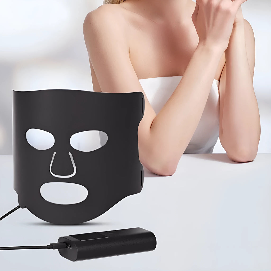 Black and white LED phototherapy face mask with controller and strap on a table.