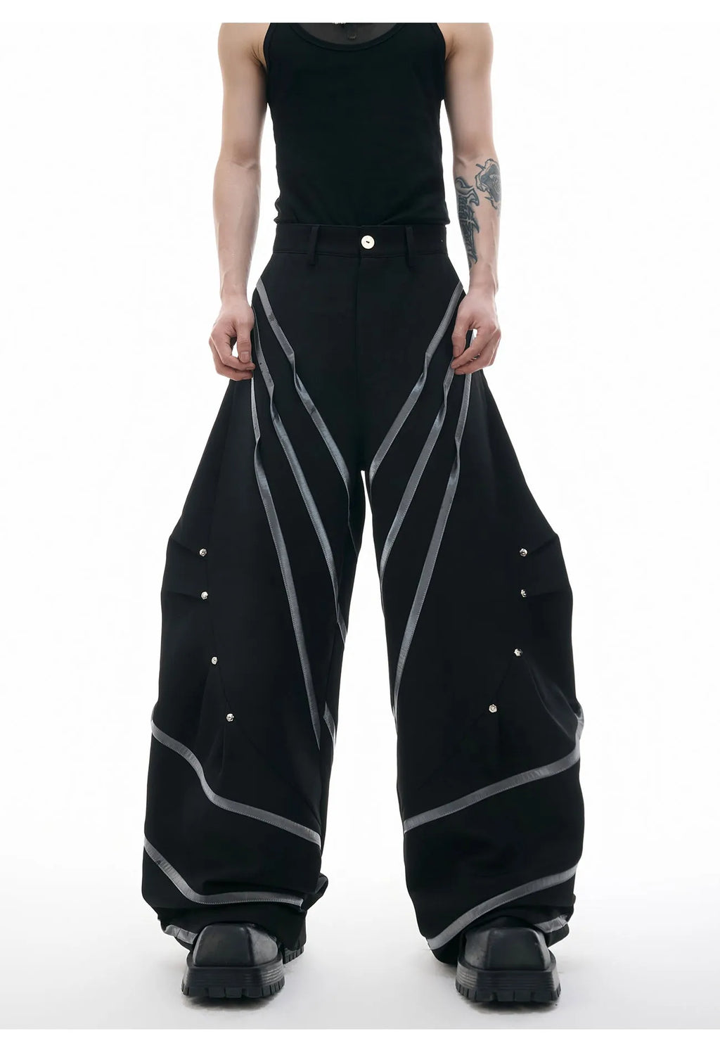 Men's black trousers with white pleated detail and silver metal striped rivets, showing the three-dimensional cut.