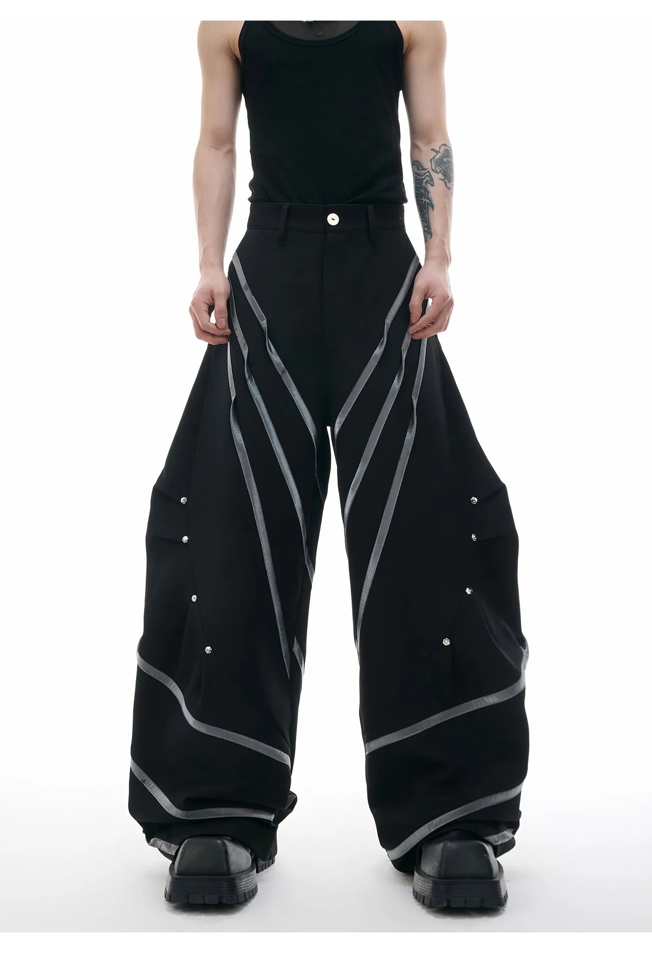 Men's black trousers with white pleated detail and silver metal striped rivets, showing the three-dimensional cut.