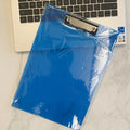 Transparent A4 plate writing board holder with metal clip, shown in blue colour on a desk.