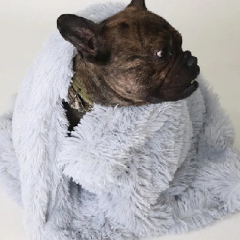 Soft grey long plush pet blanket for dogs on a wooden floor next to a kennel.