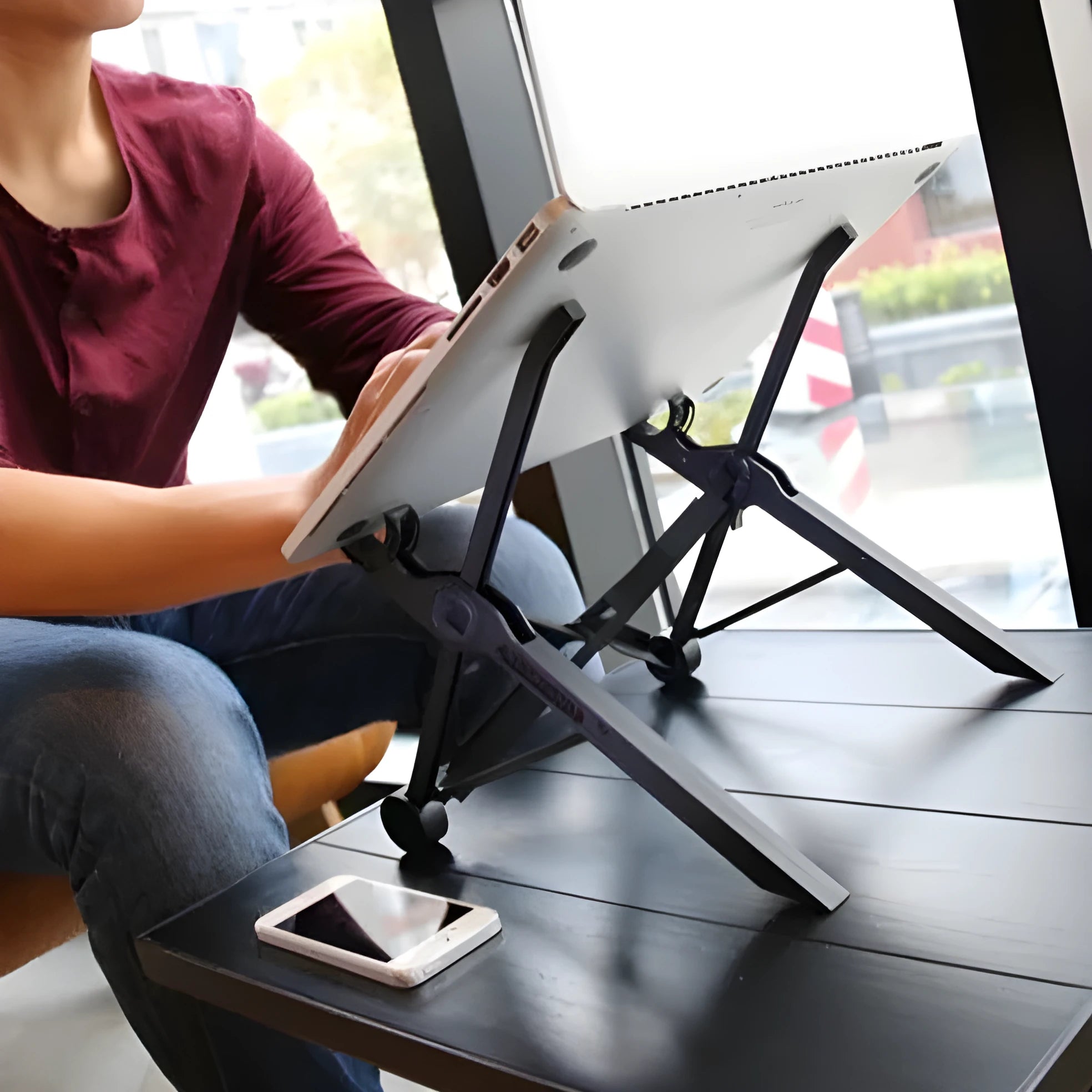 Sagacious black portable folding laptop stand with lifting function on a desk.