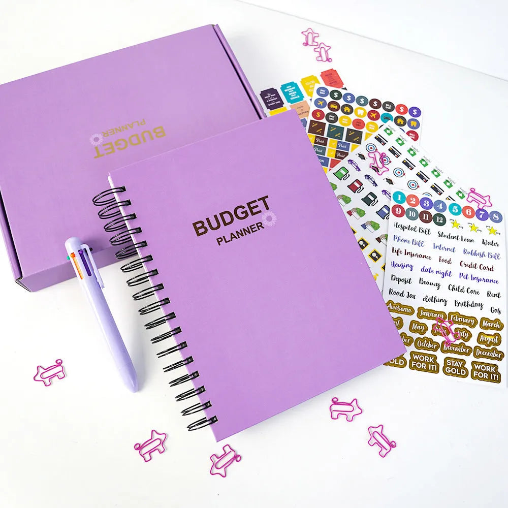 J12 Purple coil-bound monthly financial planning notebook with pen, stickers, and paper clips on a desk.