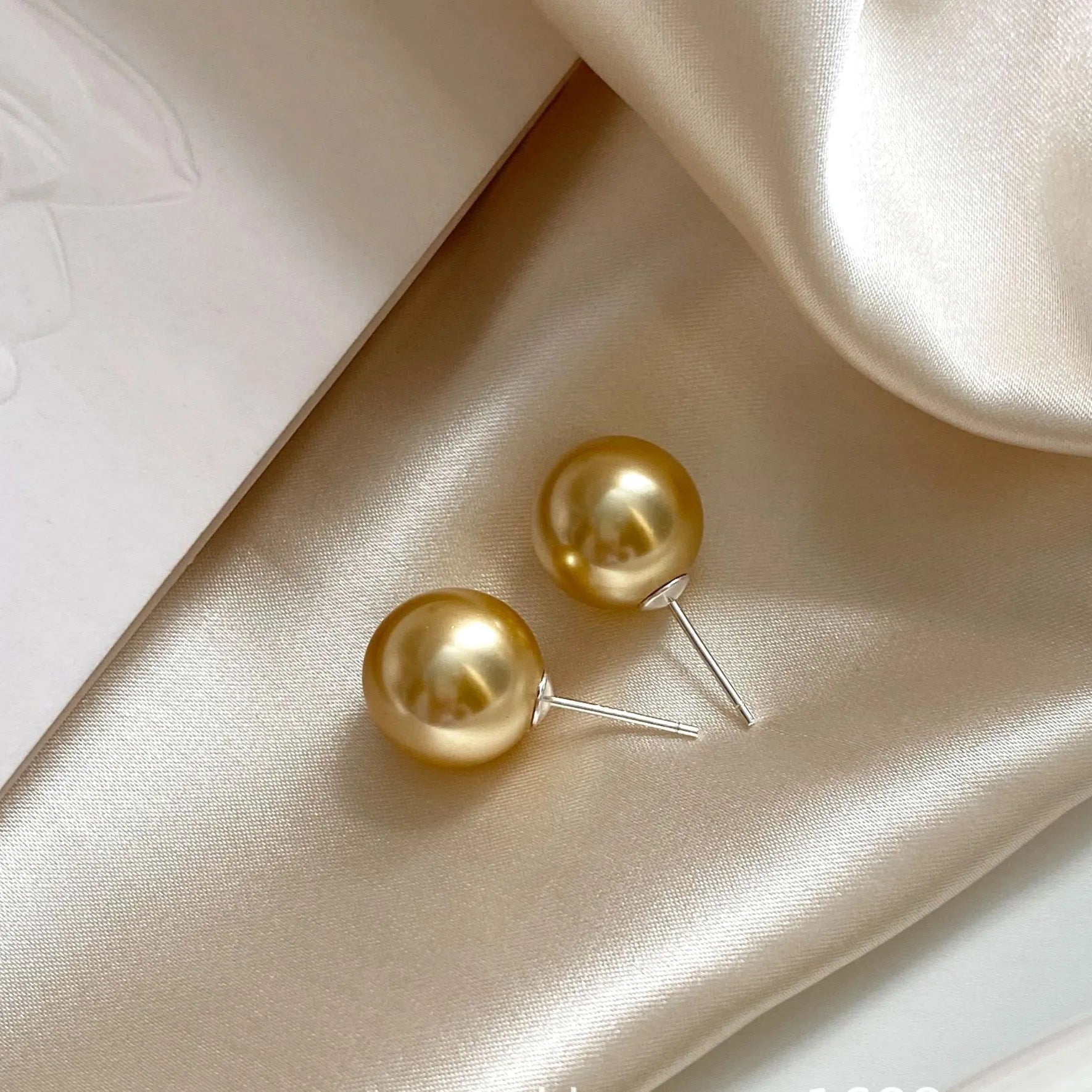 A pair of large pearl stud earrings with a geometric silver setting on a white background.