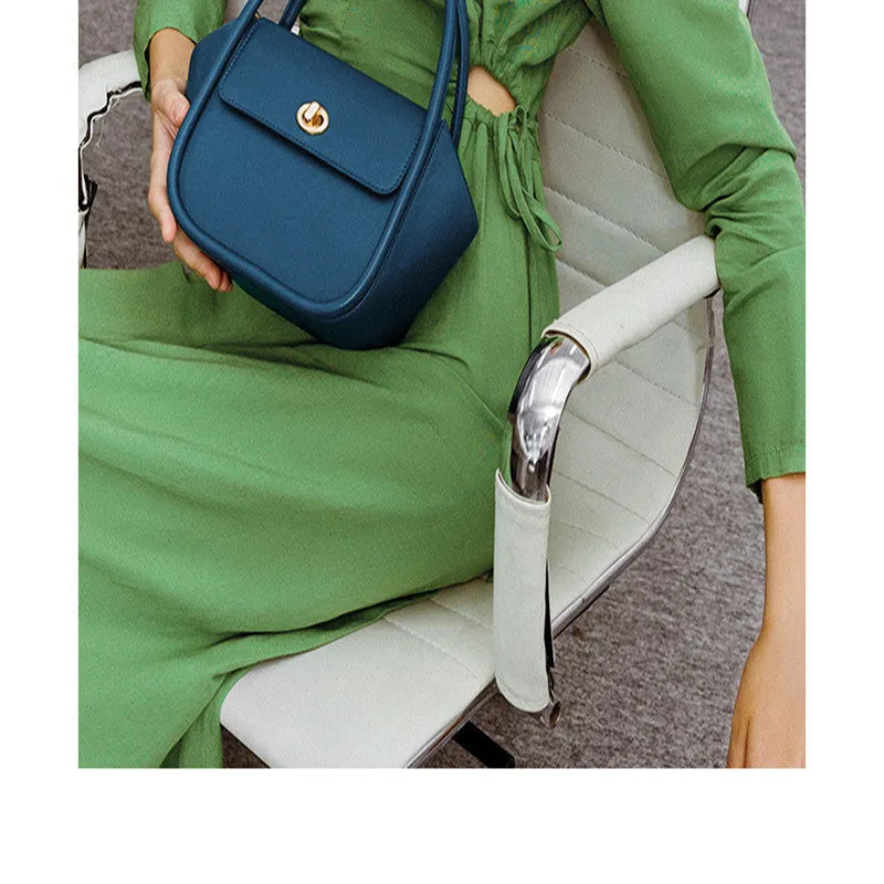 Brown leather wing-shaped tote bag with a buckle detail and latch closure, shown with a single cross-body strap.
