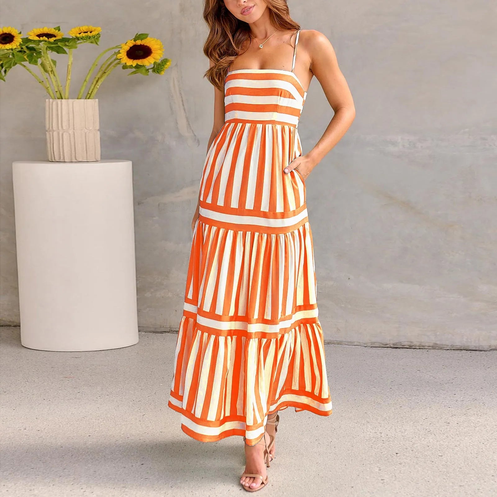 Woman wearing a striped backless suspender long dress with a square neck and side pockets.
