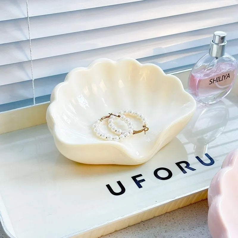 White or pink plastic shell-shaped soap dish with raised design on a bathroom counter.