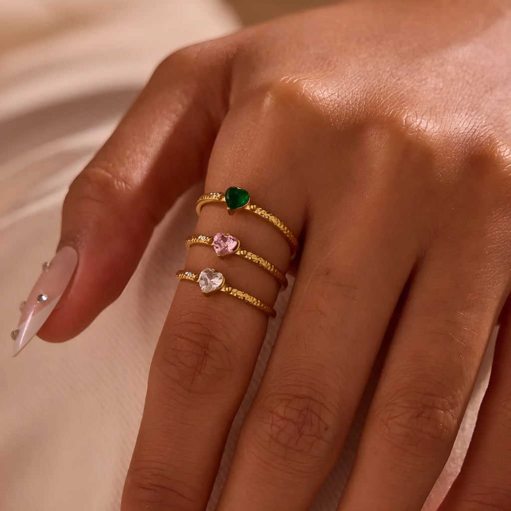 Open-ended geometric stainless steel ring with a green zircon heart inlay on a grey background.