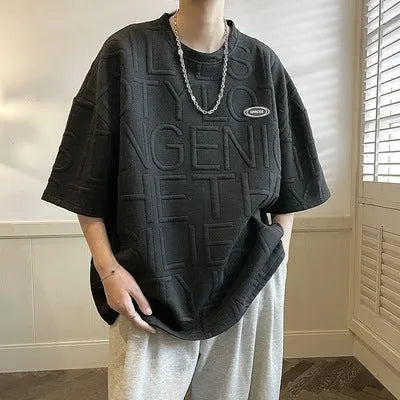 Men's grey short sleeve T-shirt with a raised 3D letter pattern, shown in a loose retro fit.