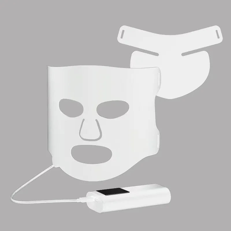 Black and white LED phototherapy face mask with controller and strap on a table.