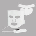 Black and white LED phototherapy face mask with controller and strap on a table.