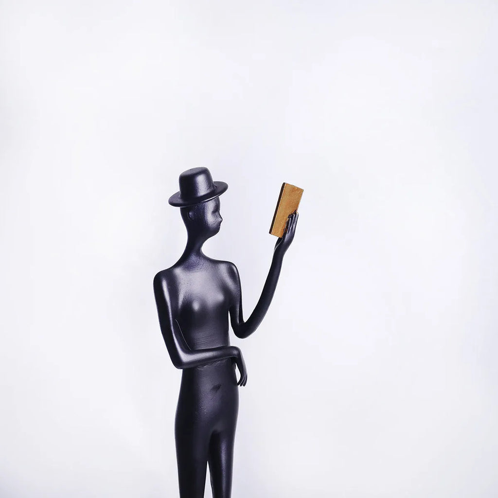Black cast aluminium sculpture of a woman reading, modern minimalist desk decor.