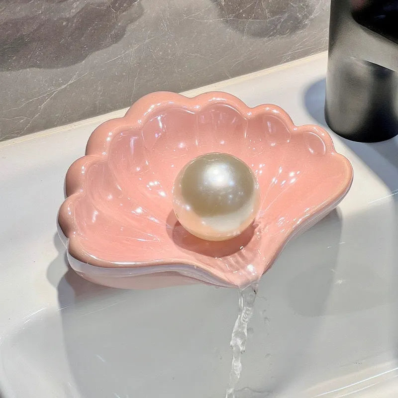 White or pink plastic shell-shaped soap dish with raised design on a bathroom counter.