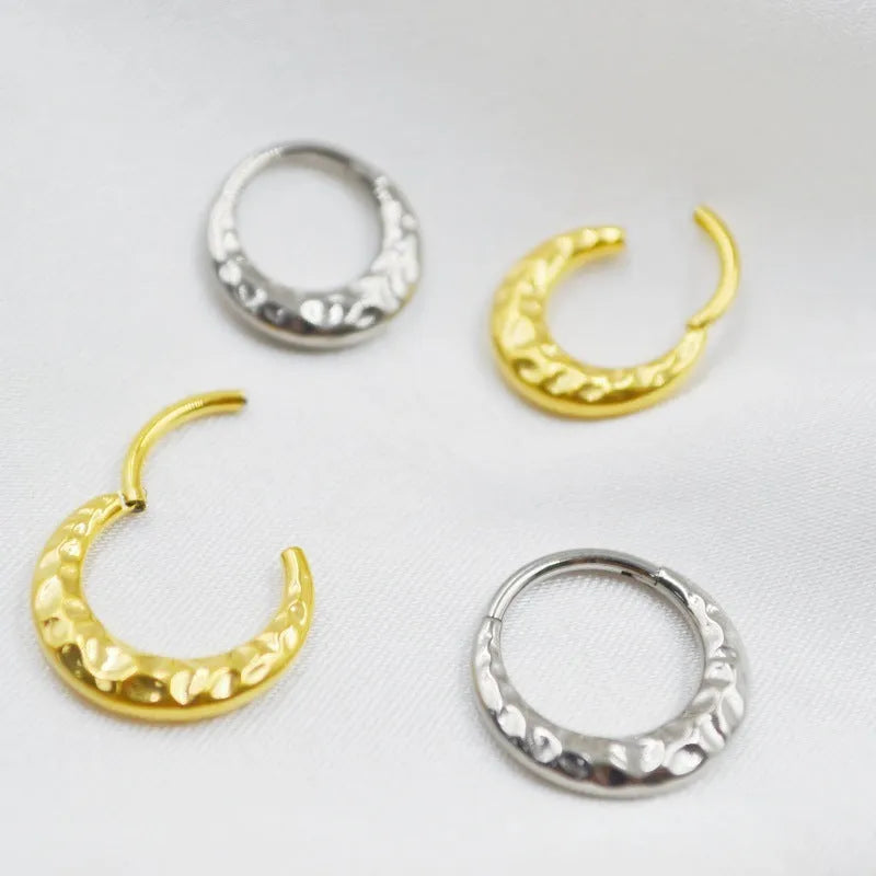 Close-up of a titanium concave-convex nose ring in gold, showing its carved texture and circular shape.