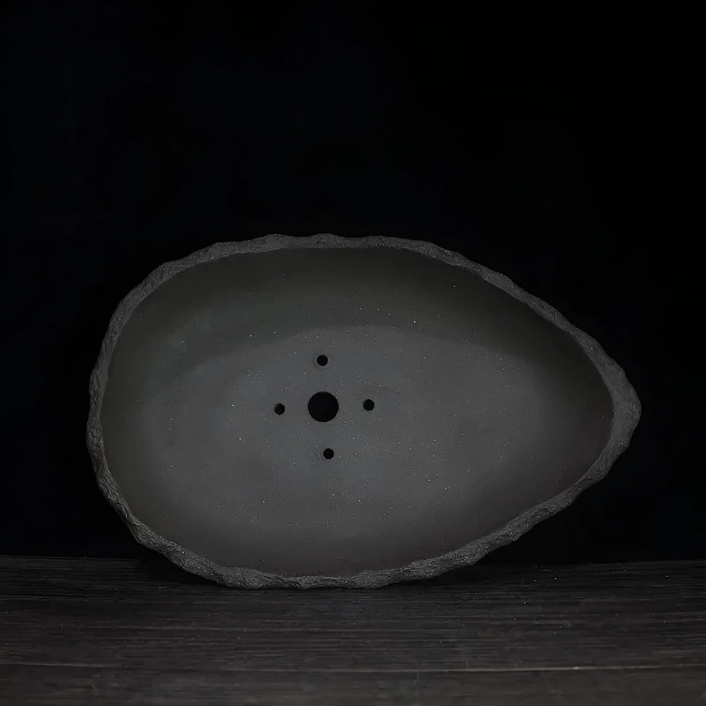 Handmade purple clay flower pot in a unique shape on a floor, showing colour and texture detail.