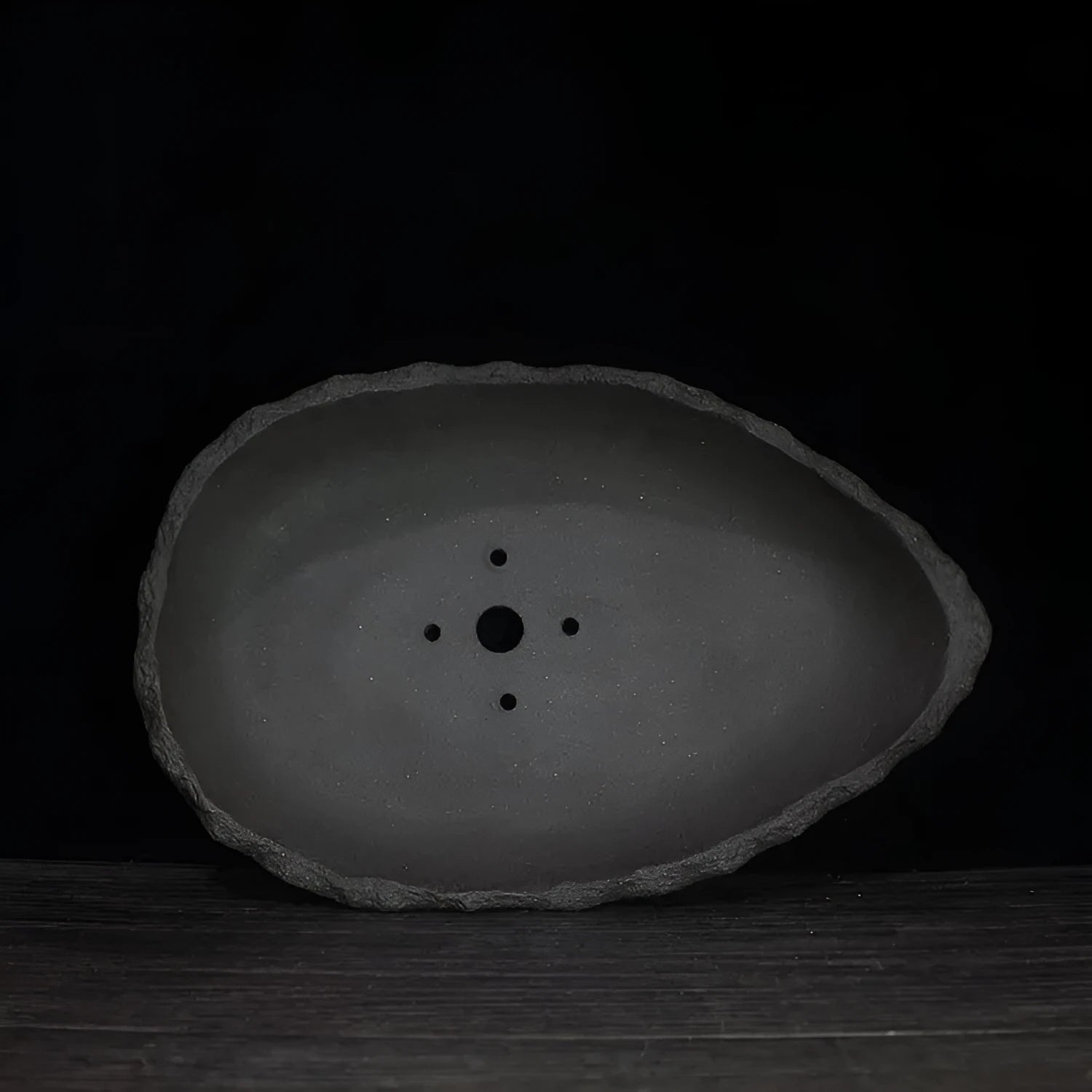 Handmade purple clay flower pot in a unique shape on a floor, showing colour and texture detail.