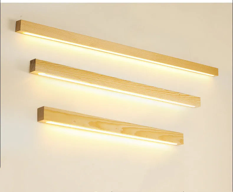 Modern walnut-coloured wood and acrylic log strip wall lamp in three lengths on a white wall.