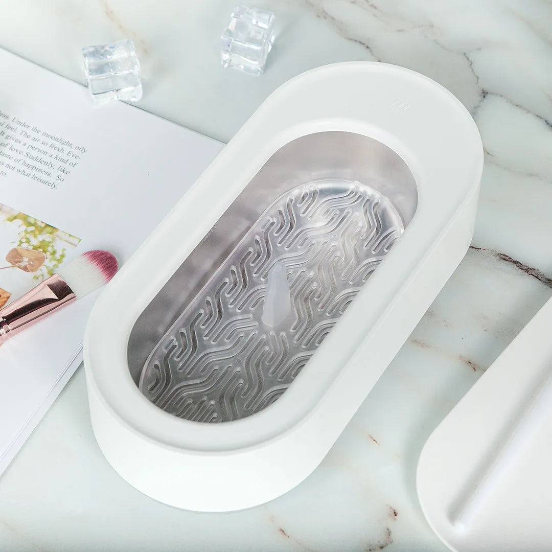 White portable ultrasonic cleaner with stainless steel tank and a single control button.