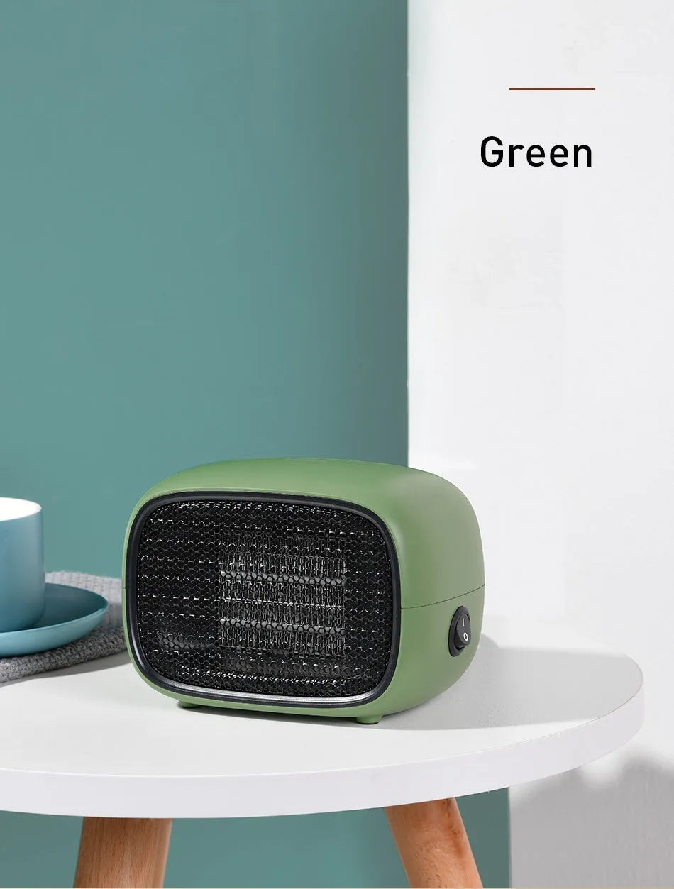 Compact green mini ceramic desk heater with metal mesh front grille, shown next to a pen for scale.