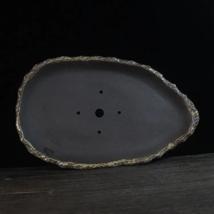 Handmade purple clay flower pot in a unique shape on a floor, showing colour and texture detail.
