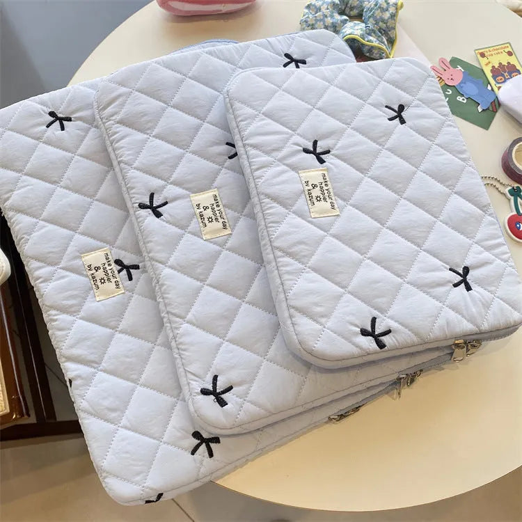 White nylon laptop bag with embroidered rhombus pattern and fabric bow, shown alongside black, light blue, and light pink colour options.