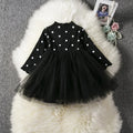 Baby girl wearing a long sleeve black tutu lace dress for a first birthday or christening event.